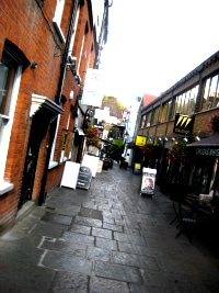 A narrow Hampstead side street lined with shopfronts and A-boards on wet paving