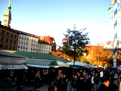 A crowded open-air market in Munich under striped awnings in low autumn sun