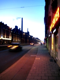 A Munich street at dusk, a car blurring past lit shopfronts