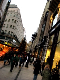 A Budapest shopping street at dusk, lit shopfronts and a Christmas tree among the crowd