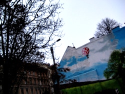 A mural of a hot-air balloon painted on the gable end of a Budapest building, bare branches in front of it